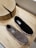 A pair of casual slip-on shoes is placed on a wooden surface. One shoe is black and the other is gray. They have a simple, minimalist design with labels visible on the inner sole. Nearby is a wooden object with a natural, rustic texture and visible grain.