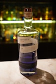 A bottle of Empress 1908 Gin on a countertop with a blurred background of various colored bottles.
