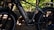 A close-up view of an electric bike with the brand name 'Fahrrbike' on the battery compartment. The bike features thick tires and a robust frame, set against a backdrop of a wooded area with dappled sunlight filtering through the trees.
