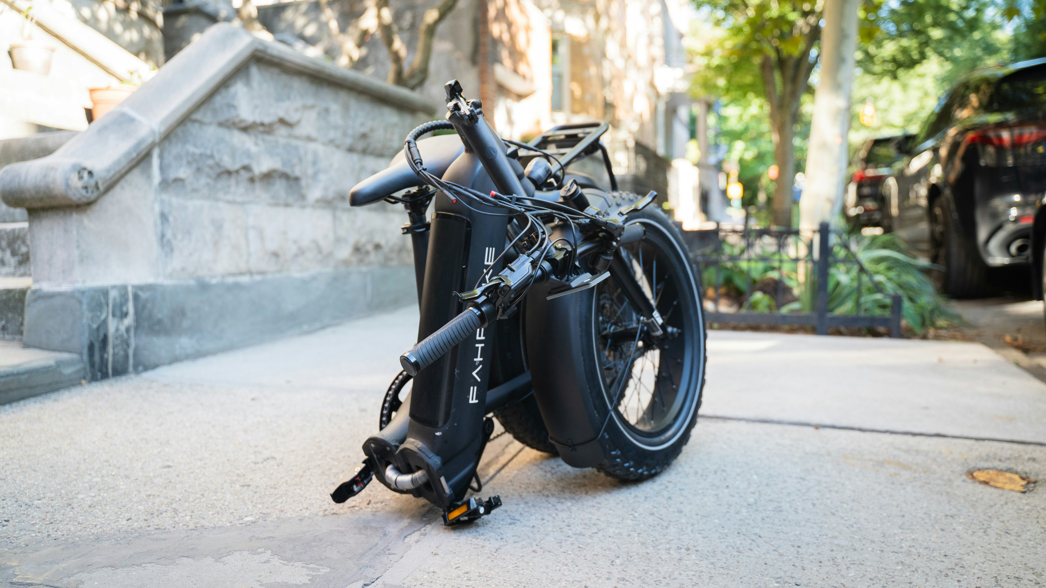 A black folding electric bicycle rests on a concrete sidewalk.
