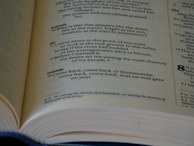 A close-up of an open book displaying text in a poetic format with multiple sections and line numbers, indicating a structured and possibly religious or literary content.