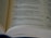 A close-up of an open book displaying text in a poetic format with multiple sections and line numbers, indicating a structured and possibly religious or literary content.