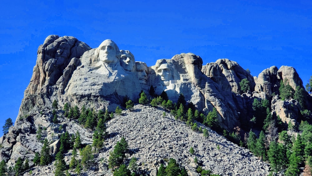 una montaña rocosa con árboles con el Monumento Nacional del Monte Rushmore al fondo