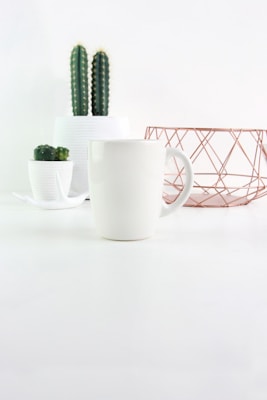 Minimalist shot of lifestyle accessories like a woven basket and ceramic mug on a soft neutral-toned table.