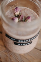 A softly lit scene showing a berry body scrub in a glass bowl with a wooden spoon and fresh berry sprigs.
