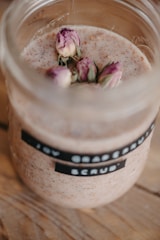 A jar containing a mixture with a creamy texture, adorned with dried rosebuds. The label on the jar reads 'grapefruit scrub.' The jar is placed on a wooden surface.