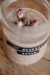 A small bowl of coarse sugar scrub with a wooden spoon resting beside it on a marble surface.