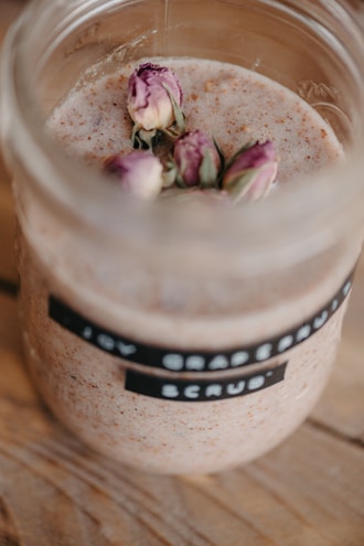 A collection of natural exfoliating scrubs in glass jars on a wooden table
