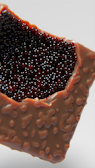 A close-up view of a partially opened chocolate bar filled with dark, glossy spheres that resemble caviar. The chocolate has a textured surface with a milky brown color, while the spheres are dark red to black and appear shiny.