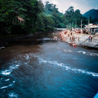 Crowded riverbank with locals and tourists under heavy rain clouds.