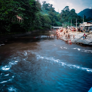 Crowded riverbank with locals and tourists under heavy rain clouds.