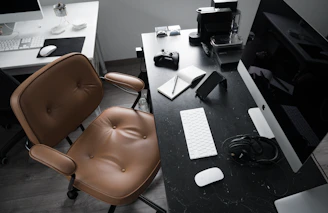 A modern workspace featuring a white desk with a black sforu handbag and a laptop, highlighting everyday luxury.