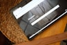A tablet resting on a woven straw mat displays a website with a clean layout featuring a large image of a tree branch with a shadow against a concrete wall. The browser toolbar and tabs are visible, indicating an open page on Unsplash.