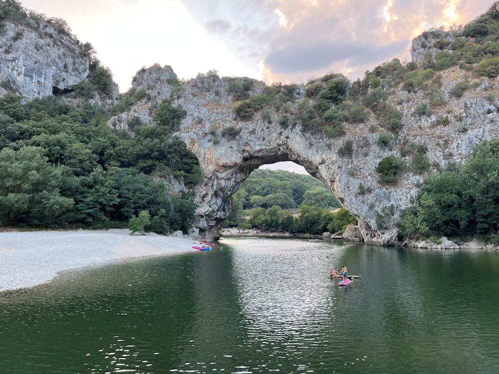 Un gruppo di persone in una barca in uno specchio d'acqua con un grande arco di roccia nel