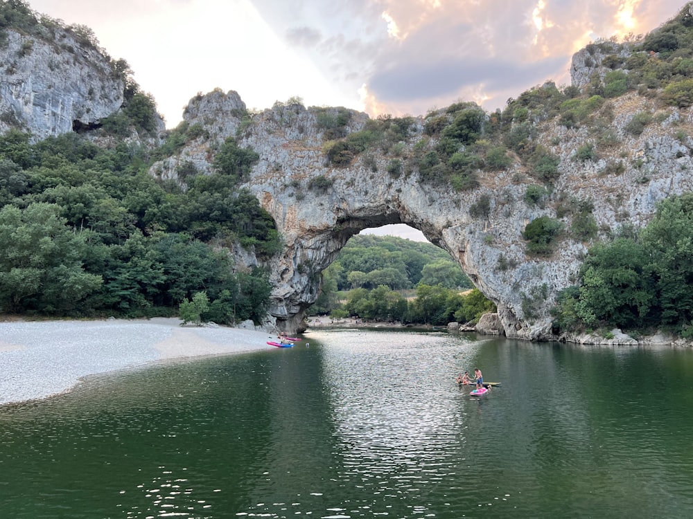 a group of people in a boat in a body of water with a large rock arch in the