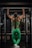 A person is performing a pull-up in a gym, wearing a matching green athletic outfit. The setting includes typical gym equipment with a focus on the muscular back and arms of the individual.