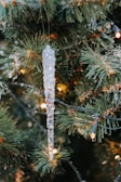 Close-up of delicate glass ornaments hanging from pine branches dusted with snow.