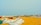 A sandy beach is populated with several fishing boats lined up along the shoreline. The ocean waves are gently hitting the shore in the background. In the foreground, fishing nets and other gear are spread out on the sand, suggesting a coastal fishing community.