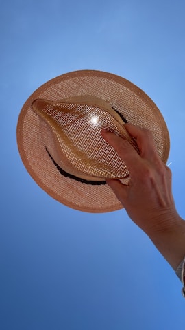 A close-up of a hand holding a soft wool hat with delicate stitching, sunlight highlighting its texture.