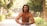 A muscular man is posing shirtless in a wooded outdoor area, flexing his biceps with a confident expression. Trees and greenery line the path, creating a peaceful, natural setting.