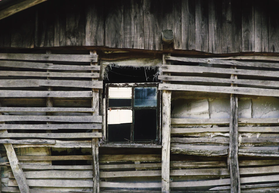 Dilapidated wooden building with significant roof damage and structural compromise visible