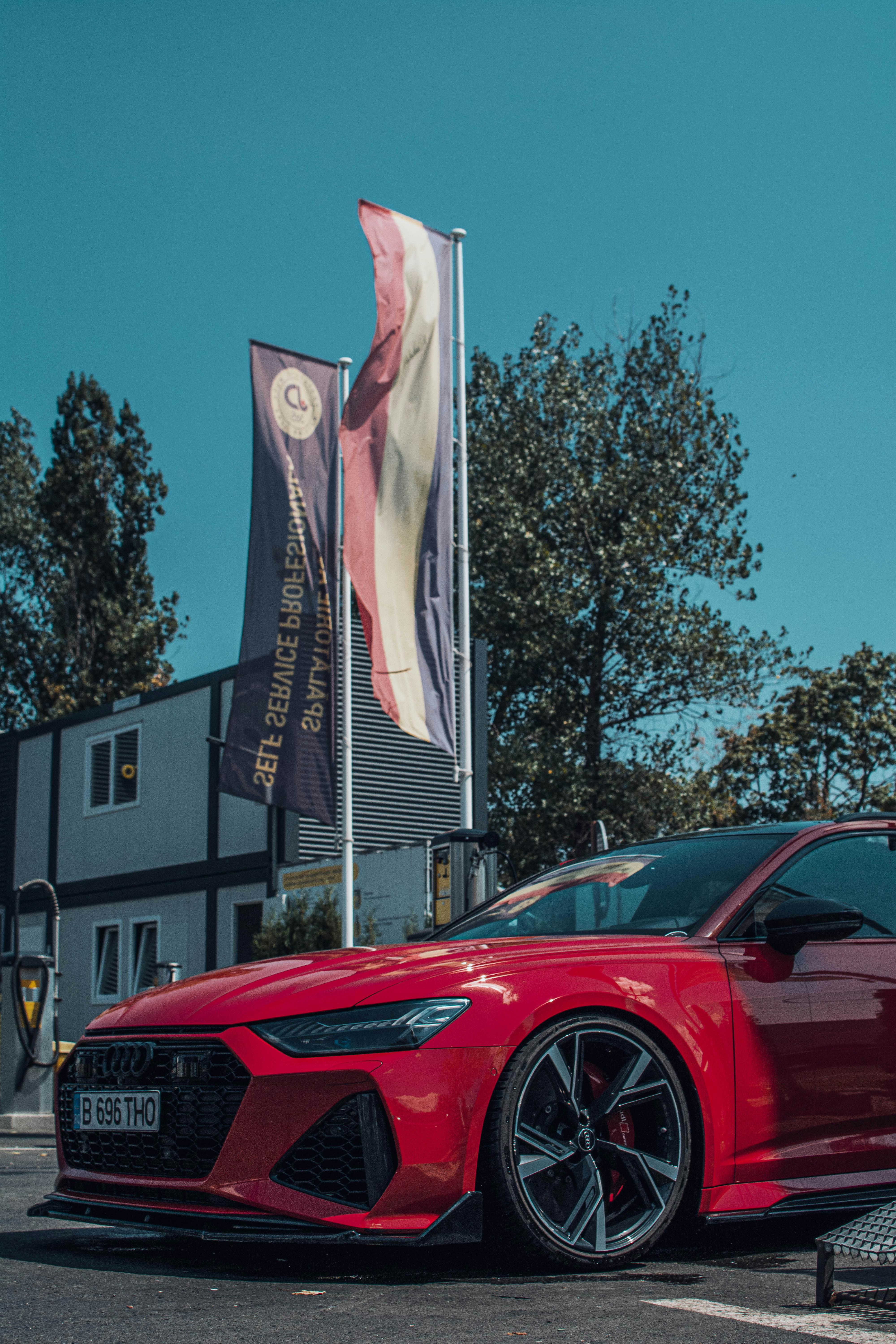 Un auto deportivo rojo estacionado frente a un edificio con una gran bandera