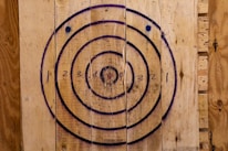 A wooden target board with concentric circles, numbered from one to four. The circles are outlined in black and blue, painted on roughly textured wooden planks, which have a natural brown color.
