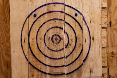 A wooden target board with concentric circles, numbered from one to four. The circles are outlined in black and blue, painted on roughly textured wooden planks, which have a natural brown color.