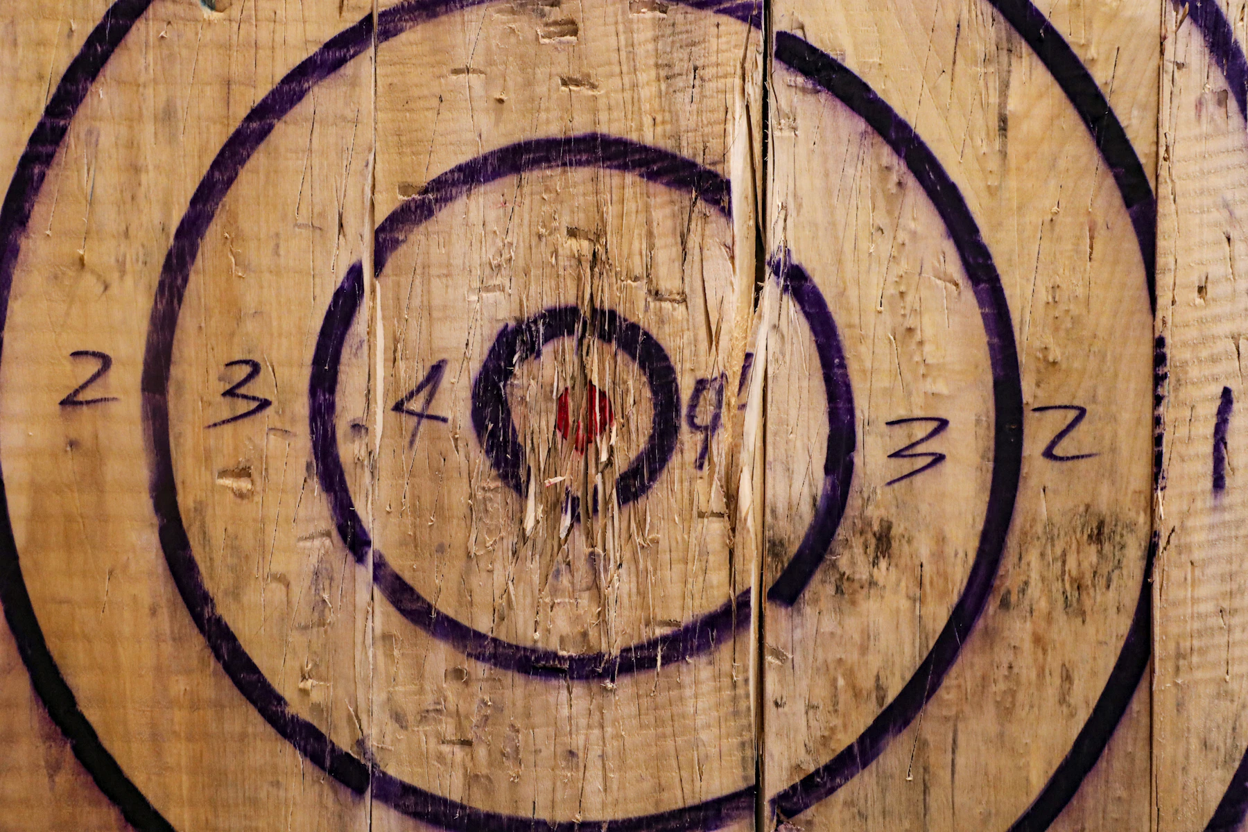 Close-up of a scarred wooden axe-throwing target with hand-drawn scoring rings numbered two to four