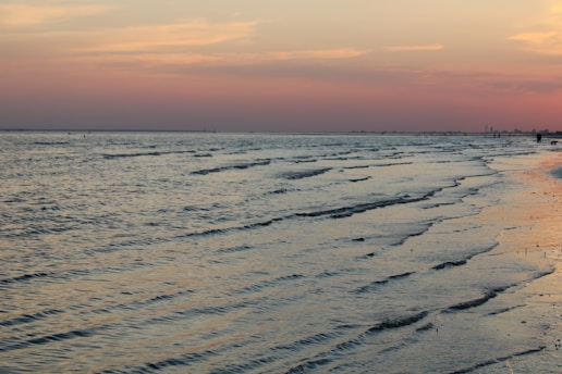 A serene beach at sunset with gentle waves and a colorful sky.