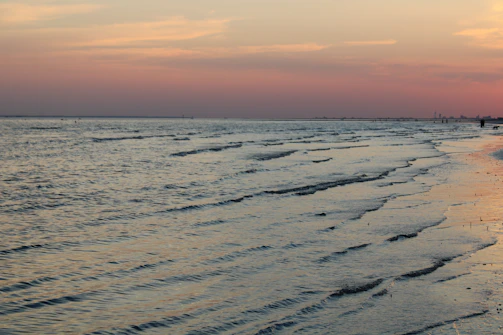 A serene beach at sunset with gentle waves and a colorful sky.