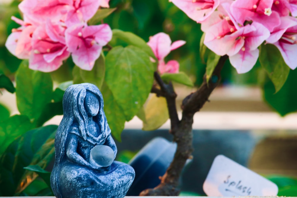 a blue figurine on a branch with pink flowers