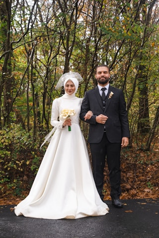 A couple dressed in wedding attire standing together in a lush forest surrounded by flowers.