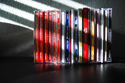 Stack of classic rock and metal CDs with neon purple lighting casting shadows on a black surface