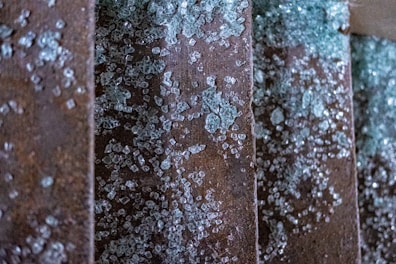 Several metal surfaces are covered with broken glass shards, glistening in various lighting conditions and appearing in scattered patterns on a rusty background.
