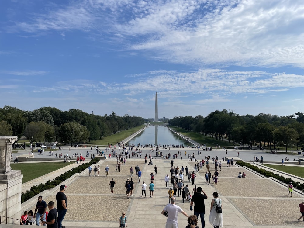 a group of people walking on a paved area with a tall tower in the background with National Mall in the background