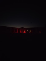 An eerie nighttime shot of a remote military base with faint red lights glowing in the fog.