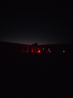 An eerie nighttime shot of a remote military base with faint red lights glowing in the fog.
