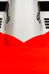 A close-up of a sleek, aerodynamic vehicle surface featuring a bold red and white color scheme. The logo of 'Shell' is prominently displayed on the smooth, glossy surface. The composition highlights the curves and design elements of the vehicle.