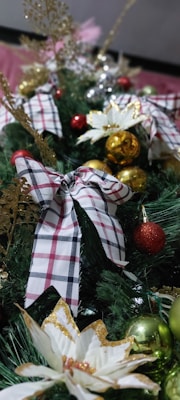 An arrangement of Christmas decorations featuring plaid ribbons, gold and red baubles, and sparkling floral ornaments atop green foliage. Gold and silver accents add to the festive theme.