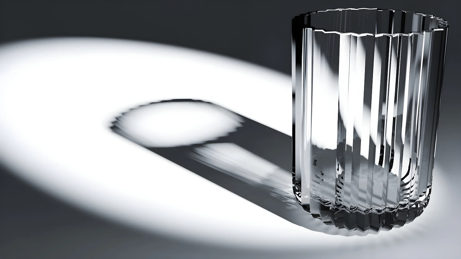A fluted tumbler in a pool of hard light, its ribs repeated in its shadow