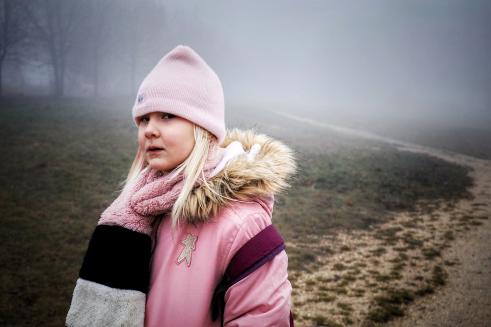 a person wearing a pink coat and hat standing on a hill