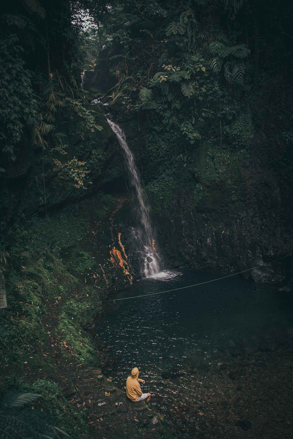 a person sitting on a rock by a stream with a fire in the middle