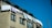 A residential building with several windows and a slanted roof has laundry hanging out to dry on a line. The sky is clear and deep blue, creating a contrast with the beige facade of the building.
