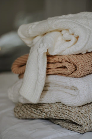 A cozy beige storage bag filled with seasonal sweaters, sitting on a soft rug.