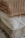 Three folded knitted sweaters stacked on top of each other in neutral tones. The top sweater has a brown ribbed pattern, the middle one is cream with a cable knit design, and the bottom sweater is beige with a thick knit texture.