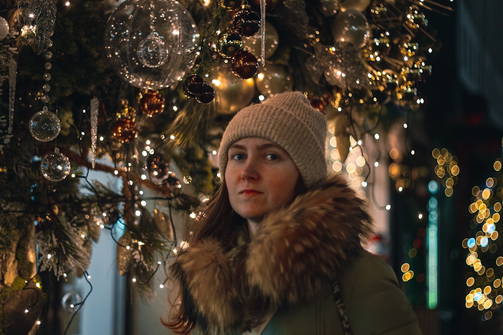 a person wearing a fur hat and scarf standing next to a christmas tree