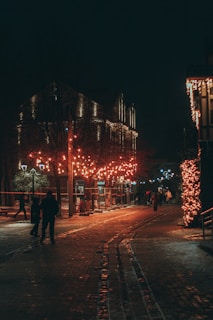 A warmly lit neighborhood street at dusk, homes adorned with colorful holiday lights glowing softly, symbolizing hope and community spirit.