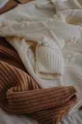 A collection of knitted sweaters in beige and cream colors, overlapping each other. The textures are prominently ribbed and feature a cozy pattern.