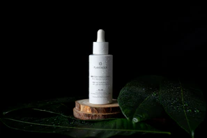 Soft focus image of the product bottle with droplets of oil glistening, surrounded by earthy green leaves